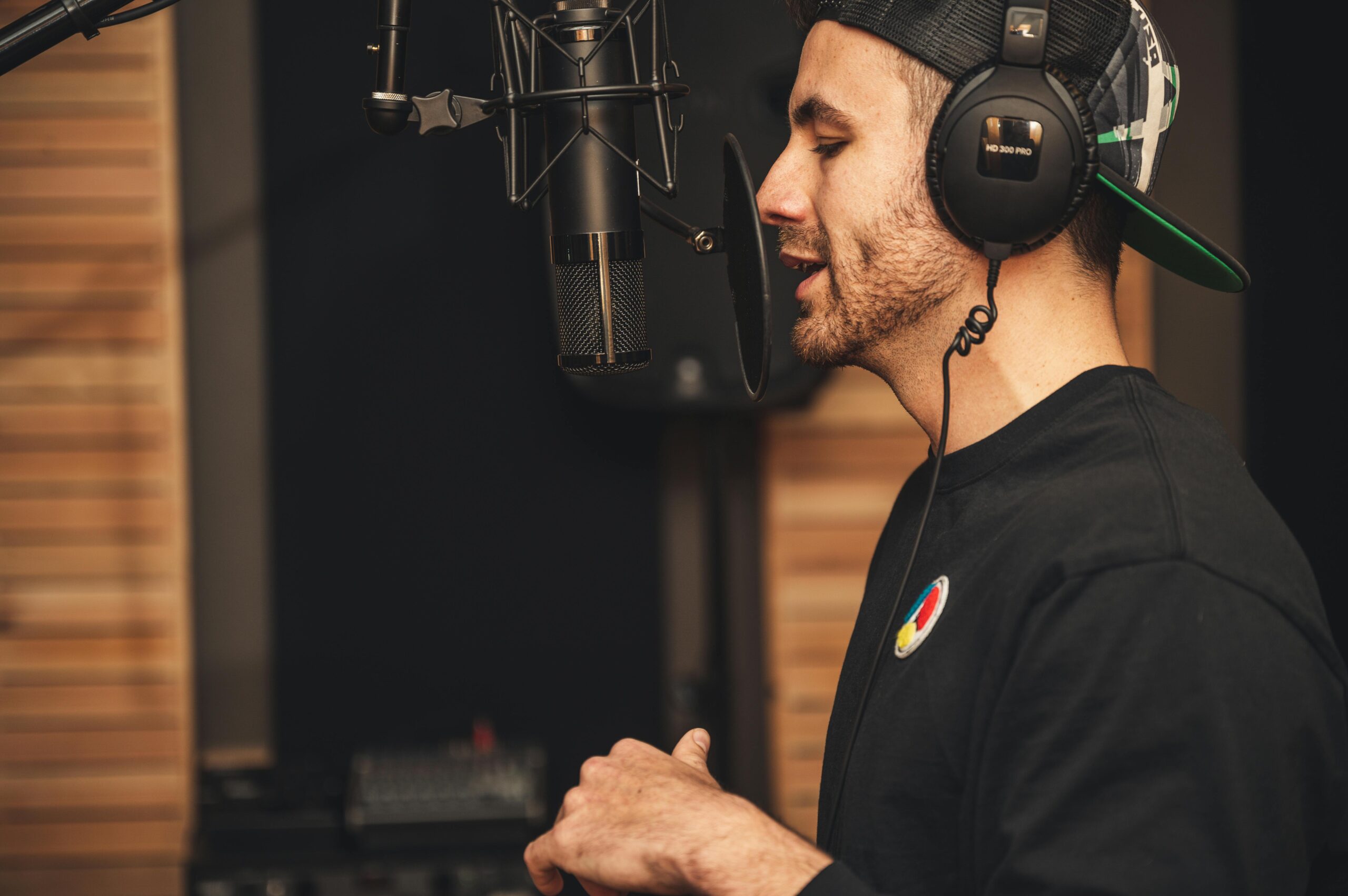 A man wearing headphones and recording vocals in a music studio with a microphone.